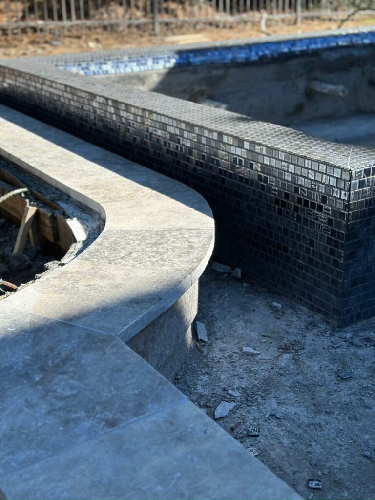Magnolia Ranch Project - Roman-style pool with infinity edge spa, pillow-top edge, water features – three bubblers, six deck jets, French pattern travertine decking, chipping mat, artificial turf with putting green, accent boulders