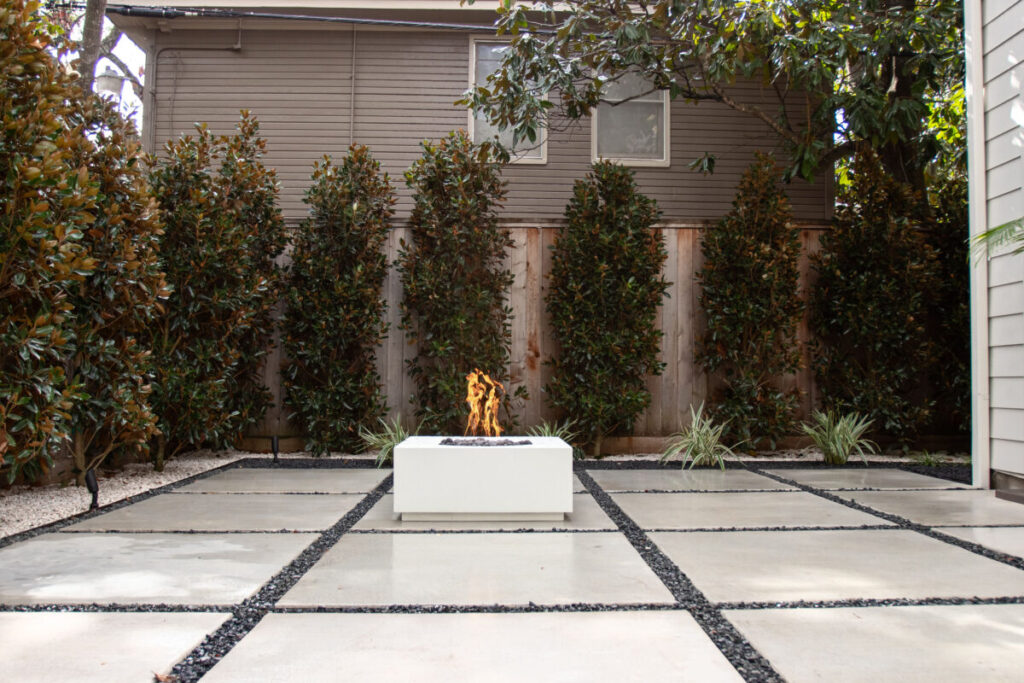 Heights Project Banks St - Poured-in-place concrete pavers, hardscaping, landscaping, Little Gem magnolia,, bamboo 'Graceful', Japanese yew, flax lily, black star gravel, white gravel, landscape uplights, Mexican heather, variegated liriope, sweet alyssum, metal planter, seasonal flowers, metal border built in-house, welded on-site, elegant white precast firepit