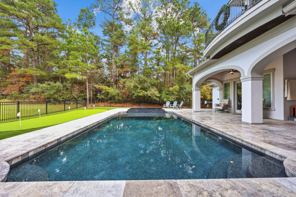 Magnolia Ranch Project - Roman-style pool with infinity edge spa, pillow-top edge, water features – three bubblers, six deck jets, French pattern travertine decking, chipping mat, artificial turf with putting green, accent boulders