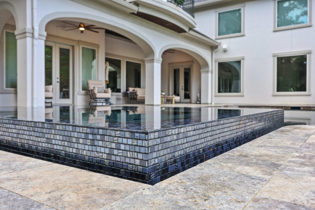 Magnolia Ranch Project - Roman-style pool with infinity edge spa, pillow-top edge, water features – three bubblers, six deck jets, French pattern travertine decking, chipping mat, artificial turf with putting green, accent boulders