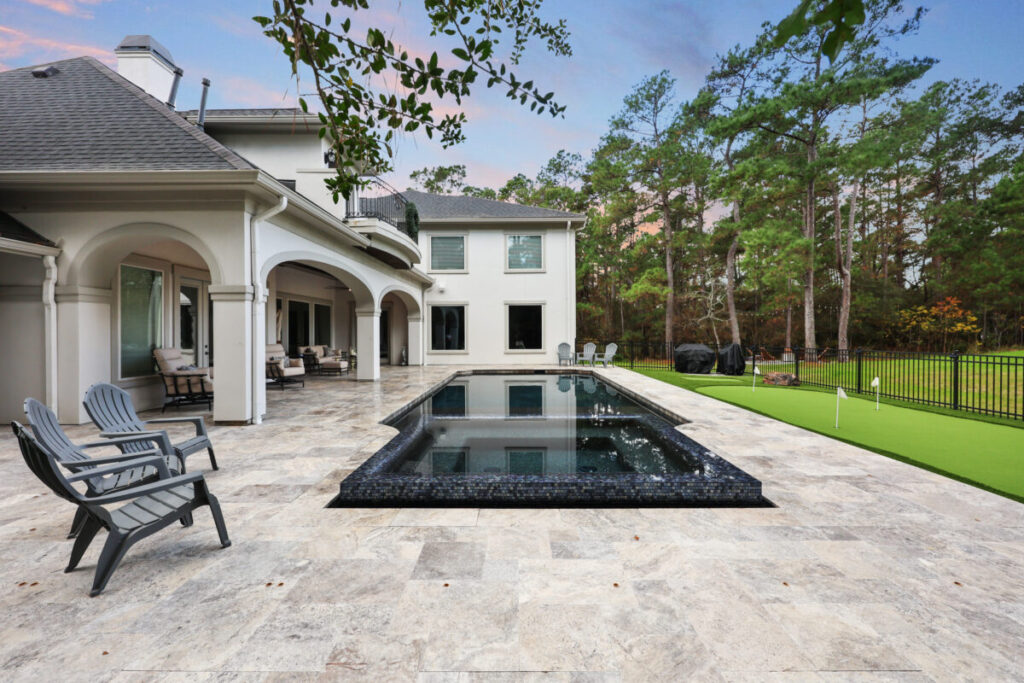 Magnolia Ranch Project - Roman-style pool with infinity edge spa, pillow-top edge, water features – three bubblers, six deck jets, French pattern travertine decking, chipping mat, artificial turf with putting green, accent boulders