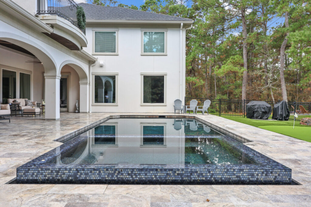 Magnolia Ranch Project - Roman-style pool with infinity edge spa, pillow-top edge, water features – three bubblers, six deck jets, French pattern travertine decking, chipping mat, artificial turf with putting green, accent boulders