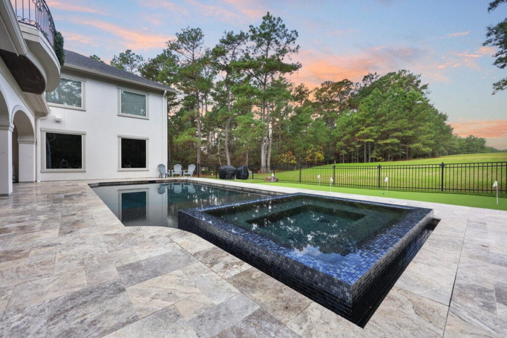 Magnolia Ranch Project - Roman-style pool with infinity edge spa, pillow-top edge, water features – three bubblers, six deck jets, French pattern travertine decking, chipping mat, artificial turf with putting green, accent boulders
