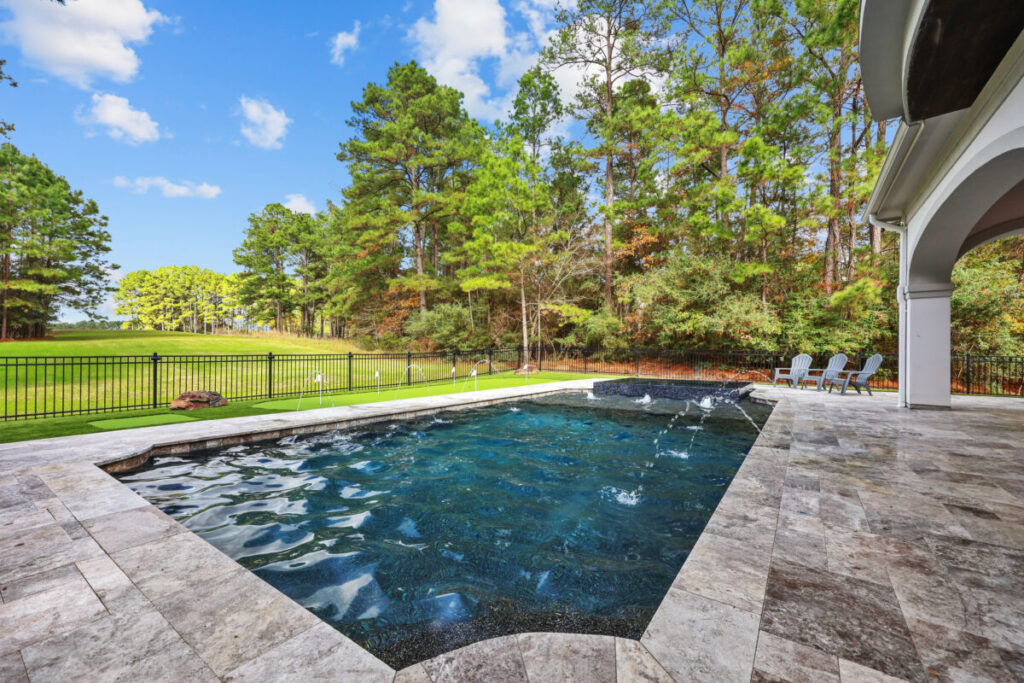 Magnolia Ranch Project - Roman-style pool with infinity edge spa, pillow-top edge, water features – three bubblers, six deck jets, French pattern travertine decking, chipping mat, artificial turf with putting green, accent boulders