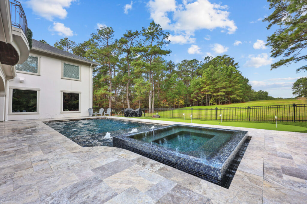 Magnolia Ranch Project - Roman-style pool with infinity edge spa, pillow-top edge, water features – three bubblers, six deck jets, French pattern travertine decking, chipping mat, artificial turf with putting green, accent boulders