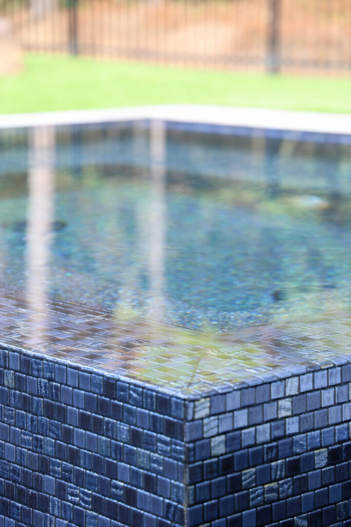 Magnolia Ranch Project - Roman-style pool with infinity edge spa, pillow-top edge, water features – three bubblers, six deck jets, French pattern travertine decking, chipping mat, artificial turf with putting green, accent boulders