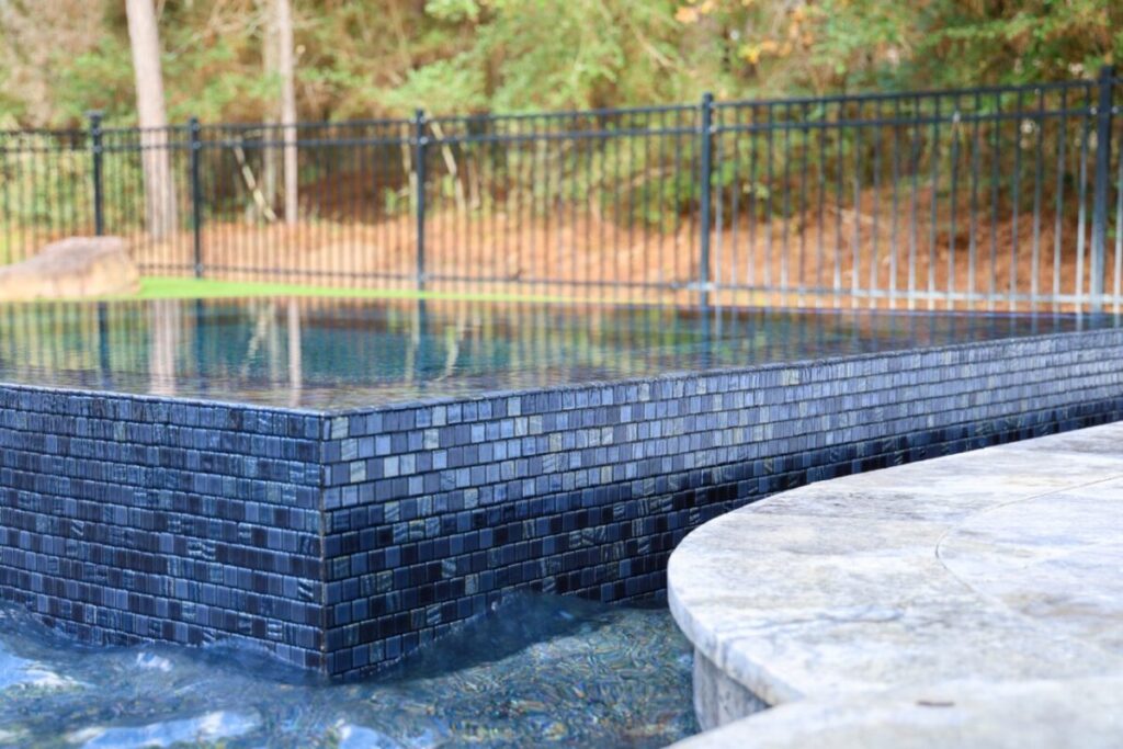 Magnolia Ranch Project - Roman-style pool with infinity edge spa, pillow-top edge, water features – three bubblers, six deck jets, French pattern travertine decking, chipping mat, artificial turf with putting green, accent boulders
