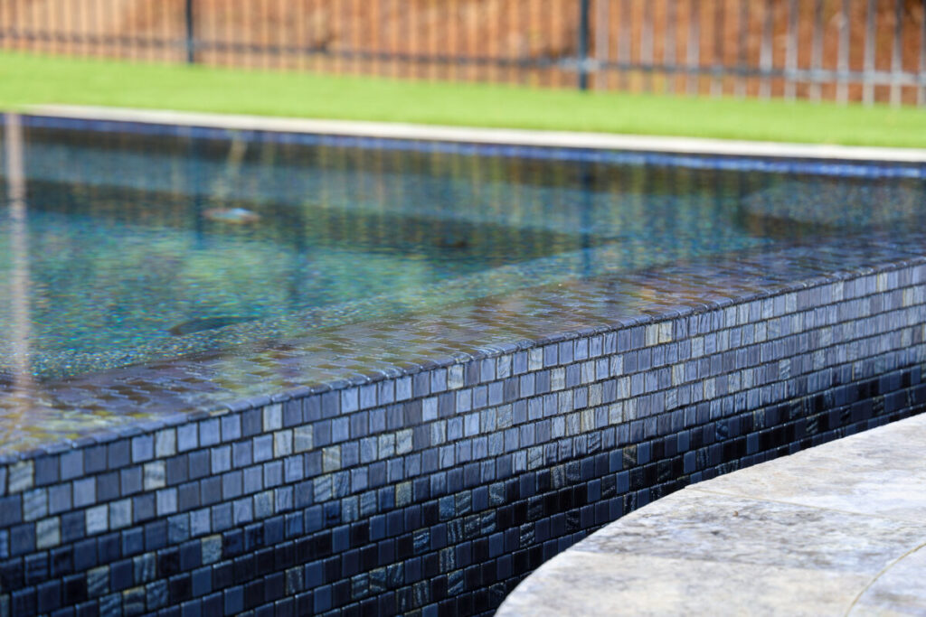 Magnolia Ranch Project - Roman-style pool with infinity edge spa, pillow-top edge, water features – three bubblers, six deck jets, French pattern travertine decking, chipping mat, artificial turf with putting green, accent boulders