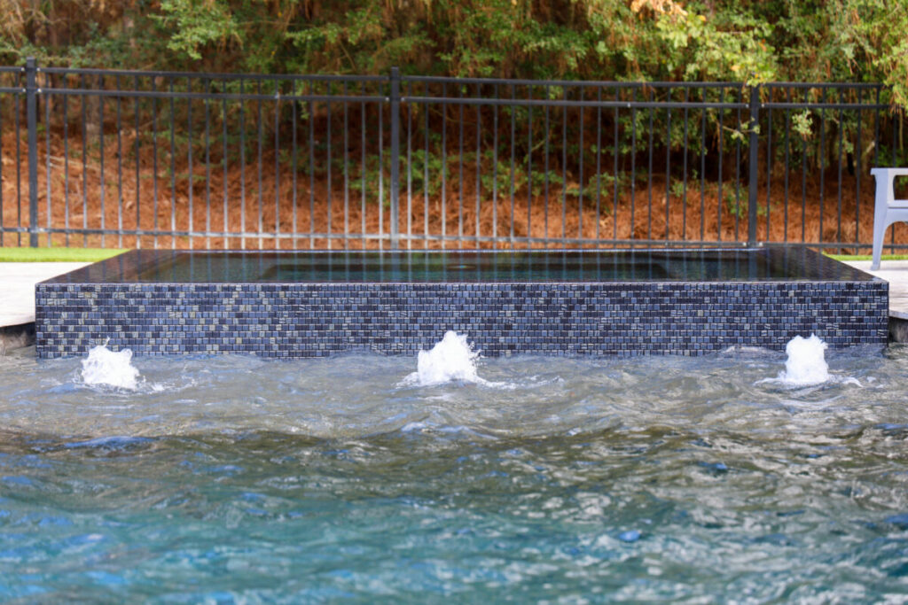 Magnolia Ranch Project - Roman-style pool with infinity edge spa, pillow-top edge, water features – three bubblers, six deck jets, French pattern travertine decking, chipping mat, artificial turf with putting green, accent boulders