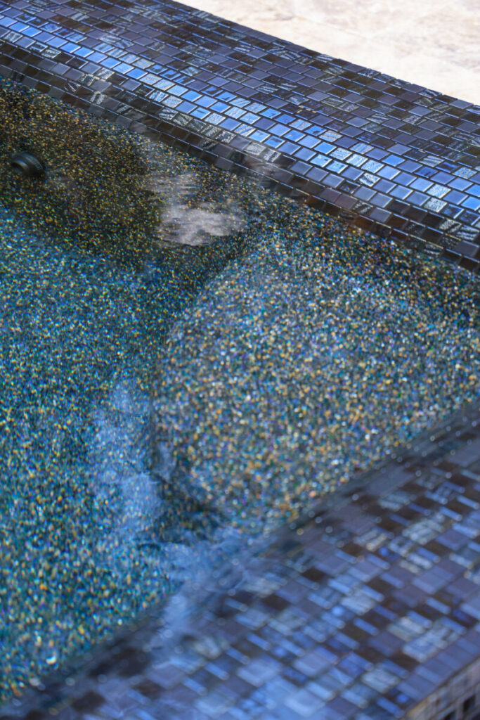 Magnolia Ranch Project - Roman-style pool with infinity edge spa, pillow-top edge, water features – three bubblers, six deck jets, French pattern travertine decking, chipping mat, artificial turf with putting green, accent boulders
