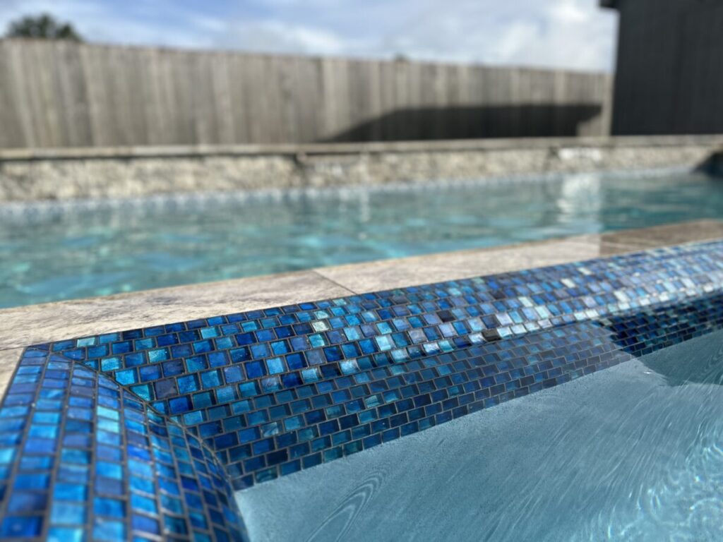 Cypress Project - Blue Wood - Geometric pool, tanning ledge, spa, safety railing, raised back wall, two fire bowls, one scupper, gas fire pit, multi-colored glass beads, travertine topper, split-face siding, glass tile, Arizona Sugar spray decking