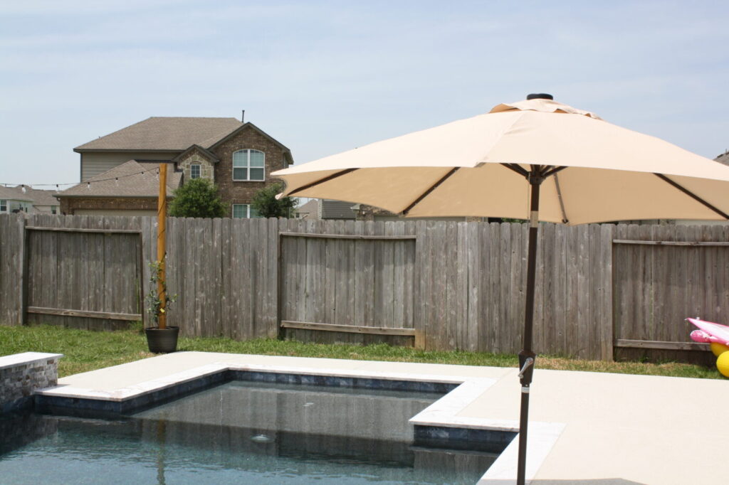 Texas Turf Tenders installed a geometric pool with a beach entry, tanning ledge, and in-water barstools. They added a raised spa with a rolled edge, a raised wall with columns and scuppers, plus surrounding turf and spray decking.