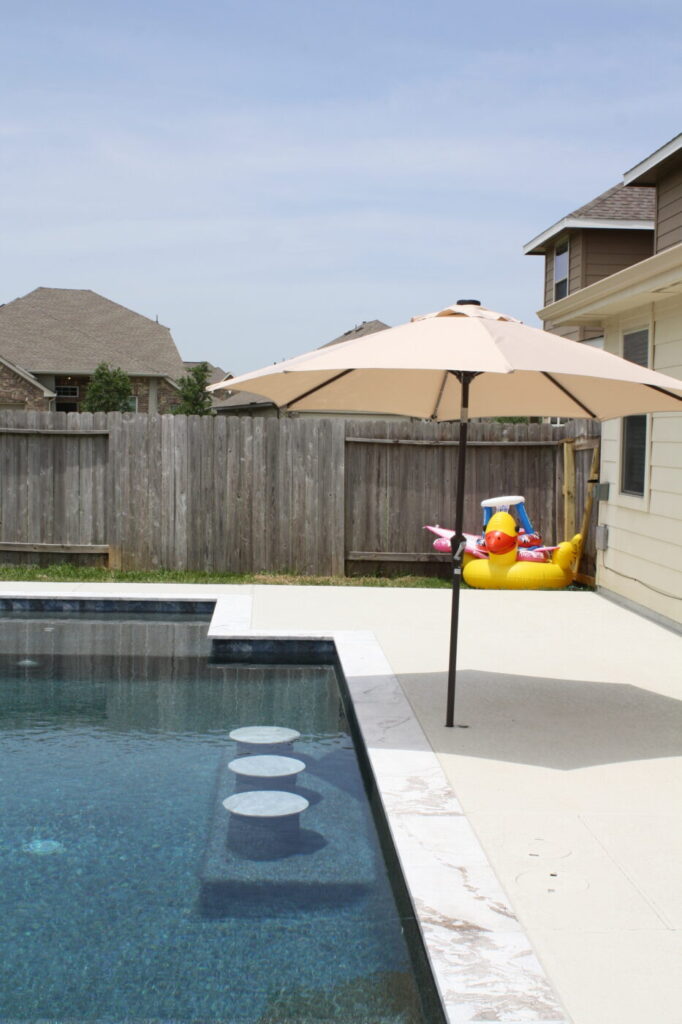 Texas Turf Tenders installed a geometric pool with a beach entry, tanning ledge, and in-water barstools. They added a raised spa with a rolled edge, a raised wall with columns and scuppers, plus surrounding turf and spray decking.