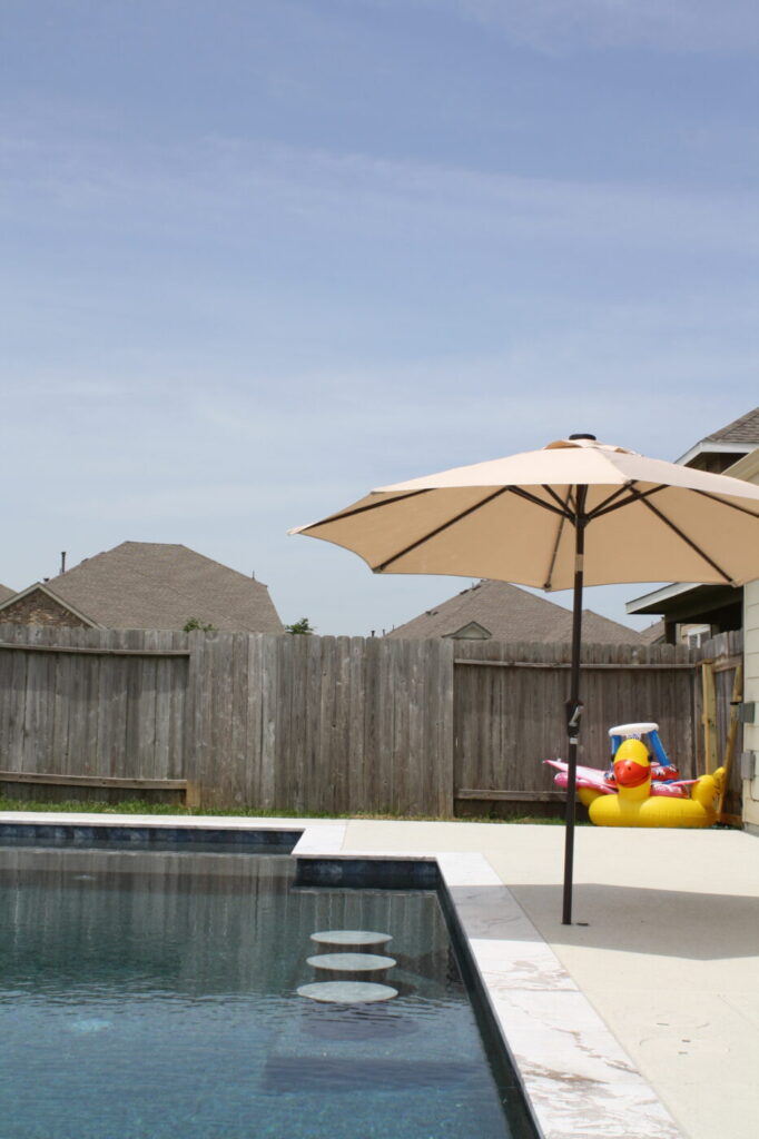 Texas Turf Tenders installed a geometric pool with a beach entry, tanning ledge, and in-water barstools. They added a raised spa with a rolled edge, a raised wall with columns and scuppers, plus surrounding turf and spray decking.