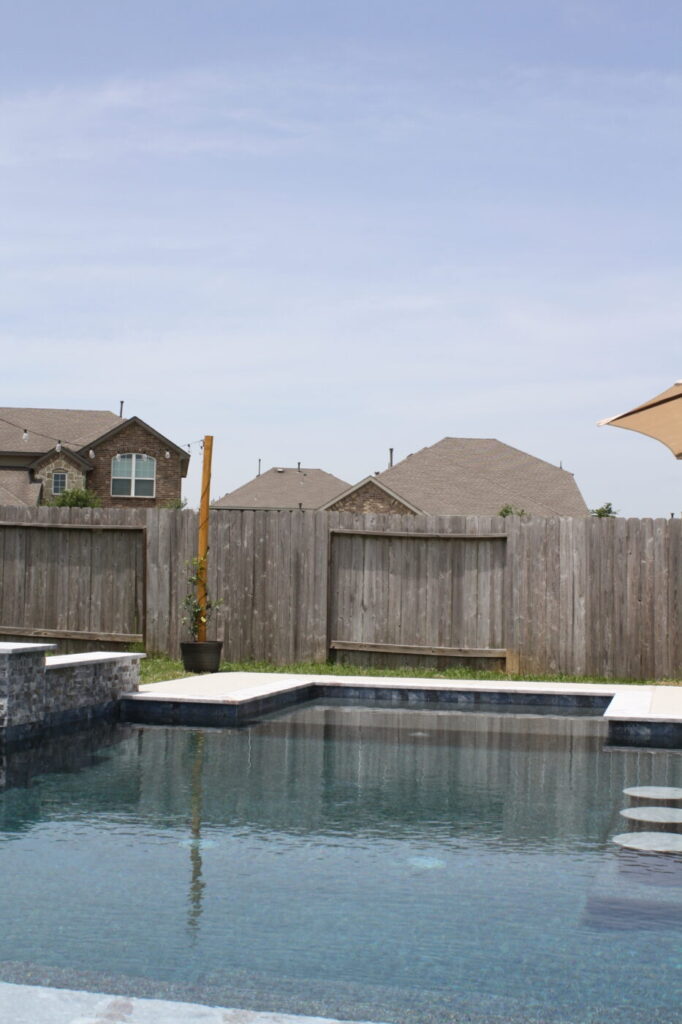 Texas Turf Tenders installed a geometric pool with a beach entry, tanning ledge, and in-water barstools. They added a raised spa with a rolled edge, a raised wall with columns and scuppers, plus surrounding turf and spray decking.