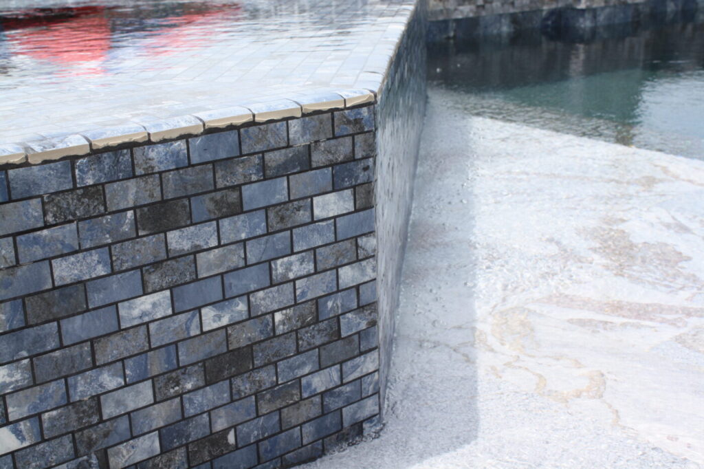 Texas Turf Tenders installed a geometric pool with a beach entry, tanning ledge, and in-water barstools. They added a raised spa with a rolled edge, a raised wall with columns and scuppers, plus surrounding turf and spray decking.