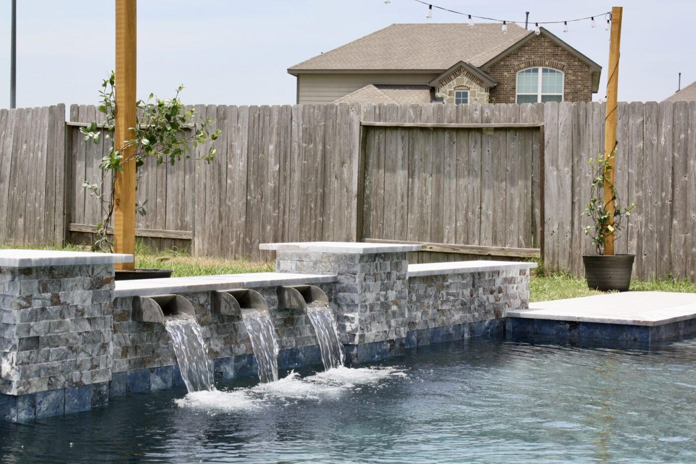 Texas Turf Tenders installed a geometric pool with a beach entry, tanning ledge, and in-water barstools. They added a raised spa with a rolled edge, a raised wall with columns and scuppers, plus surrounding turf and spray decking.