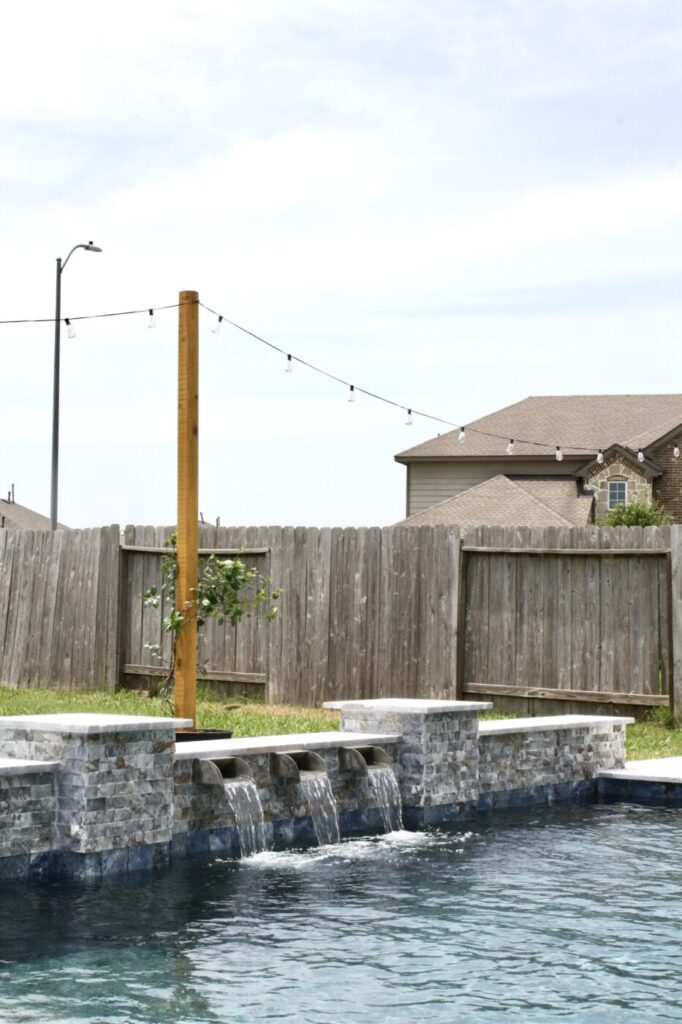 Texas Turf Tenders installed a geometric pool with a beach entry, tanning ledge, and in-water barstools. They added a raised spa with a rolled edge, a raised wall with columns and scuppers, plus surrounding turf and spray decking.
